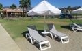 On the sandy beach near the grassy lawn and paved boardwalk are an umbrella and sun loungers made of plastic and fabric. Not far a Royalty Free Stock Photo