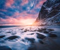 Sandy beach with stones in blurred water, colorful sky