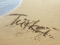 Sandy beach with wave and the word `Turkey` written in German in the sand Royalty Free Stock Photo