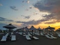 Sandy beach white lounge chairs aligned next to sea for relaxation with parasols and sunshades during sunrise with colorful sky Royalty Free Stock Photo