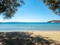 Sandy empty beach with tree shadow, moored yacht in calm sea at Greek islands, Cyclades Greece