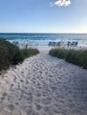 Sandy path with footprints to the beach with wild grass and blue umbrellas by the sea