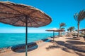 Sandy sea beach filled with sun umbrellas made of straw and sun beds on the background palm trees and blue sea. Sky with Royalty Free Stock Photo