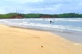 sandy seashore, in blue waves fisherman pulls out net, in distance there are green thickets of palm trees and other tropical