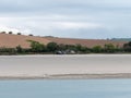 Sandy seashore on a day. Calm water surface. The remains of an old ship on the shore. A plowed field. Minimalistic landscape
