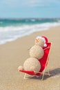 Sandy snowman in santa hat sunbathing in beach lounge.