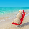 Sandy snowman in santa hat sunbathing in beach lounge.