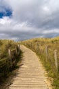 Sandy wooden footpath leads through gentle sand dunes with grasses and reeds to the beach