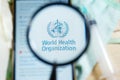 WHO World Health Organization Logo under magnifying glass with selective focus.