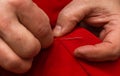 Sanior old man or woman Sews with a needle and thread at home. Fingers hands of the seamstress is using a needle and red thread to Royalty Free Stock Photo