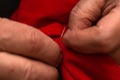 Sanior old man or woman Sews with a needle and thread at home. Fingers hands of the seamstress is using a needle and red thread to Royalty Free Stock Photo