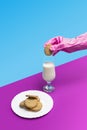 Sanitary pink glove holding a sweet cookie above a glass of milk on a pastel pink and blue background