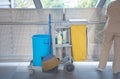 Sanitary set on tray with cleaning man, bottle of hygiene liquid with mop and bloom and bin for clean public area
