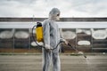 Sanitation worker in hazmat protection suit and N95 mask with chemical decontamination sprayer tank.Disinfecting streets and