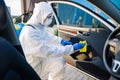 Sanitizing service worker cleans the car`s interior with a yellow rug. A man in a protective suit, mask and gloves disinfects the