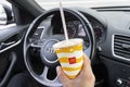 Driver hand holding McDonalds paper cup with a straw. Hand with a coca cola drink in Audi Q3 car