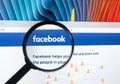 Homepage of Facebook.com on Apple iMac monitor screen under magnifying glass.