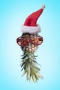 Santa ananas. Funky pop art minimal christmas in summer concept. Funny pineapple with sunglasses and santa claus hat on bright