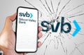 Hand holding a phone with Silicone Valley Bank website on the screen with broken glass and blurred SVB logo in the background Royalty Free Stock Photo