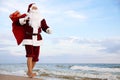 Santa Claus with bag of presents on beach, space for text. Christmas vacation Royalty Free Stock Photo