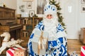 Santa Claus in a blue fur coat against the background of a garland gives a gift to the camera Royalty Free Stock Photo