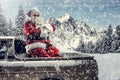 Santa Claus in a car driving to deliver some christmas presents on a sunny winter day. Blurred mountain forest background. Royalty Free Stock Photo