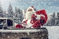 Santa Claus in a car driving to deliver some christmas presents on a sunny winter day. Blurred mountain forest background. Royalty Free Stock Photo