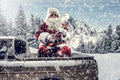 Santa Claus in a car driving to deliver some christmas presents on a sunny winter day. Blurred mountain forest background. Royalty Free Stock Photo