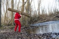 Santa Claus carrying a tree log near a lake in a forest