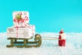 Santa Claus is carrying wooden sleigh with two gift boxes on a blue background with artificial snow. Royalty Free Stock Photo