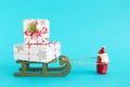 Santa Claus is carrying wooden sleigh with two gift boxes wrapped of white-gray paper, decorated of fir branch on blue background Royalty Free Stock Photo