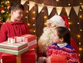 Santa Claus and child boy and girl posing together indoor near decorated xmas tree with lights, they talking, smiling and Royalty Free Stock Photo