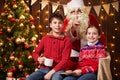 Santa Claus and child boy and girl posing together indoor near decorated xmas tree with lights, they talking, smiling and Royalty Free Stock Photo