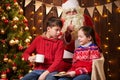 Santa Claus and child boy and girl posing together indoor near decorated xmas tree with lights, they talking, smiling and Royalty Free Stock Photo