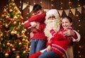 Santa Claus and child boy and girl posing together indoor near decorated xmas tree with lights, they talking, smiling and Royalty Free Stock Photo