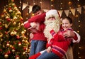 Santa Claus and child boy and girl posing together indoor near decorated xmas tree with lights, they talking, smiling and Royalty Free Stock Photo