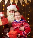 Santa Claus and child girl posing together indoor near decorated xmas tree with lights, they talking and smiling - Merry Christmas Royalty Free Stock Photo