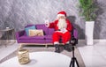 Santa Claus at Christmas recording a video with a dslr camera sitting on a couch in a modern environment