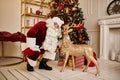 Santa Claus and deer near the fireplace and christmas tree with gifts. New year and Merry Christmas , happy holidays concept Royalty Free Stock Photo