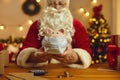 Santa Claus at desk with money and calculator holding piggy bank that`s wearing medical face mask Royalty Free Stock Photo