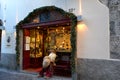 Santa Claus Dummy with a long white beard is sitting on a iron bench of a street vine store.