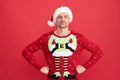 Santa Claus elf man in Christmas jumper stand confidently with arms akimbo red background, xmas