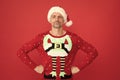 Santa Claus elf man in Christmas jumper stand confidently with arms akimbo red background, xmas