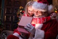 Santa Claus And Girl Opening Christmas Gift Near Christmas Tree. Child Hugging Santa. Magic Fulfillment Of Desires