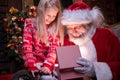 Santa Claus and girl opening Christmas gift near Christmas tree. Magic fulfillment of desires wishes