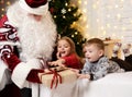 Santa Claus giving present to a happy little cute children boy and girl near Christmas tree Royalty Free Stock Photo