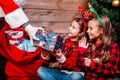 Santa Claus giving a present to two little cute sisters near Christmas tree at home Royalty Free Stock Photo