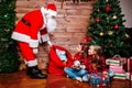 Santa Claus giving a present to two little cute sisters near Christmas tree at home Royalty Free Stock Photo