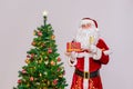 Santa Claus with a glass of sparkling wine and a gift stands next to the Christmas tree Royalty Free Stock Photo