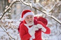 Santa claus greets in the snowy forest in December. Elderly gray-haired man in a Santa Claus costume and Christmas gift